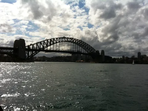 A large steel arch bridge silhouetted over a harbour under clouds