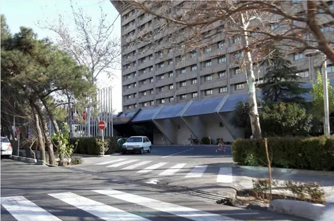 A large modern hotel building beside trees and a paved forecourt