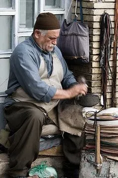 A man sitting in a shop and working with his hands beside hanging metal objects