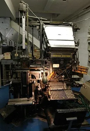 A large metal typesetting machine with a keyboard below a sloping rack