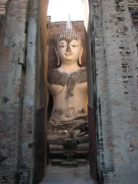 A large seated Buddha statue framed by a narrow brick doorway