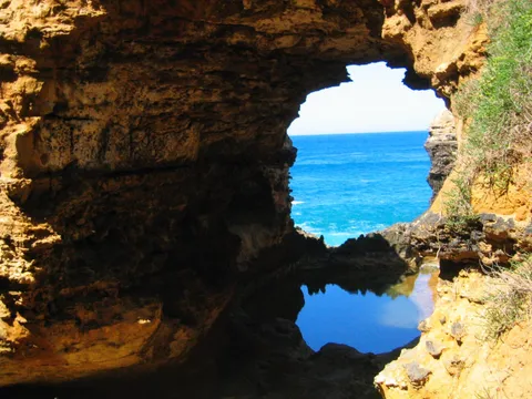 A blue ocean seen through a rocky arch above a still pool