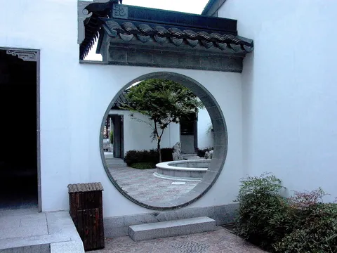 A circular doorway in a white garden wall with a tiled roof