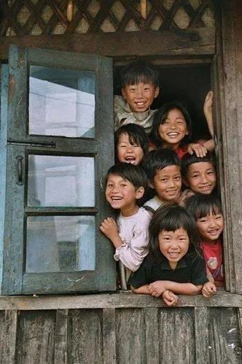 A group of smiling children leaning out of a wooden window