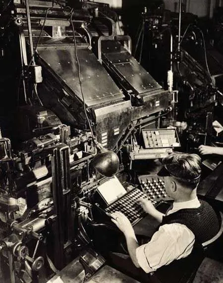A person operating a large metal typesetting machine in a workshop