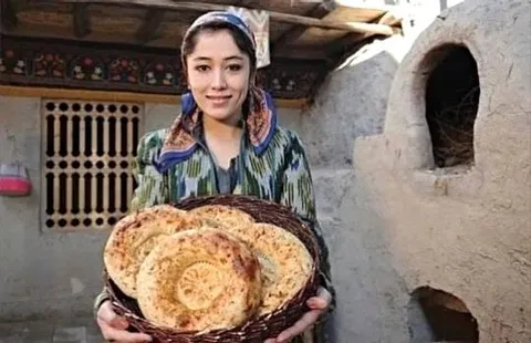 A woman holding a tray of flatbreads beside an outdoor oven