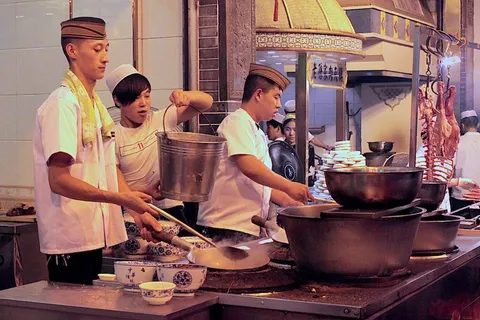 Cooks preparing food in large woks at a street stall