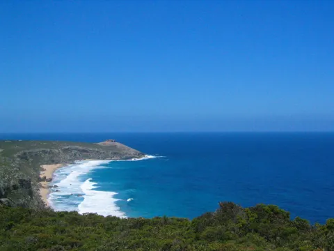 A curving sandy beach and headland beside a deep blue ocean