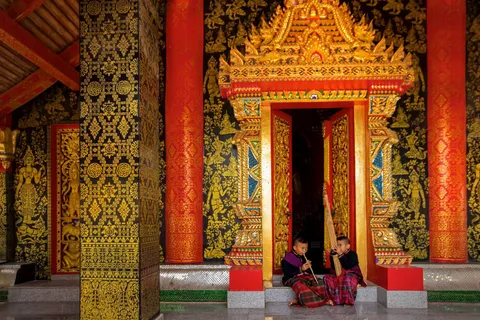 People sitting outside an ornate red and gold temple doorway