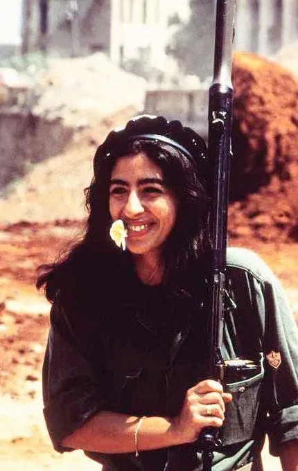 A smiling woman holding a rifle upright beside her face