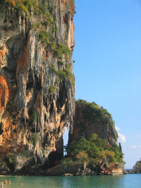 A towering limestone cliff above turquoise water with people swimming below