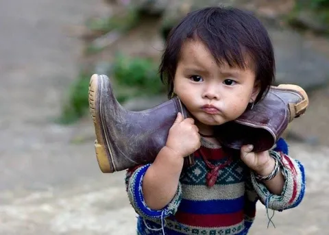 A small child holding a pair of boots over their shoulders