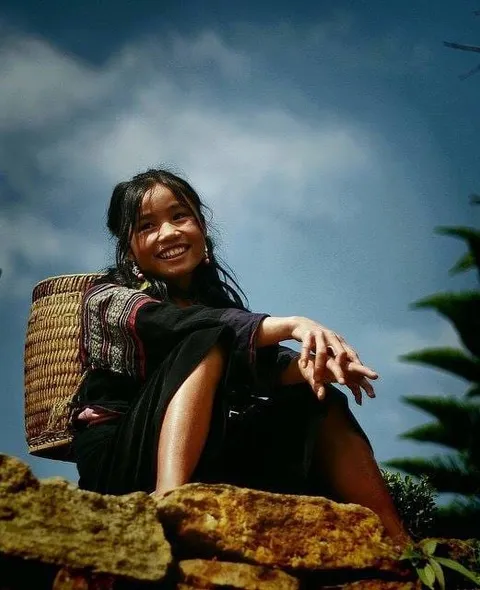 A smiling woman resting with a large woven basket on her back