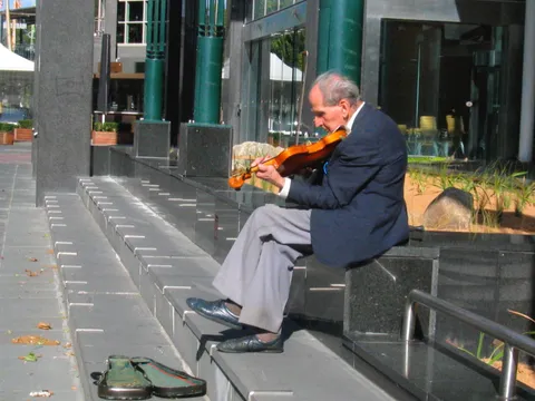 An elderly man in a suit playing a violin while seated on steps