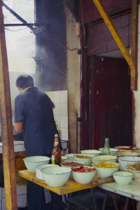 A cook beside bowls and stacked bamboo steamers in a small kitchen