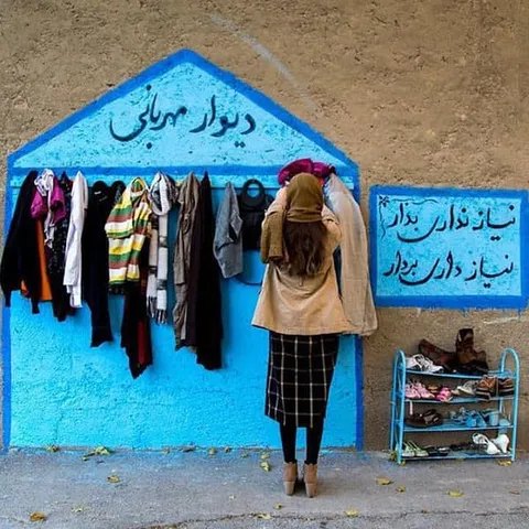 A woman hanging clothing on hooks on a bright blue wall