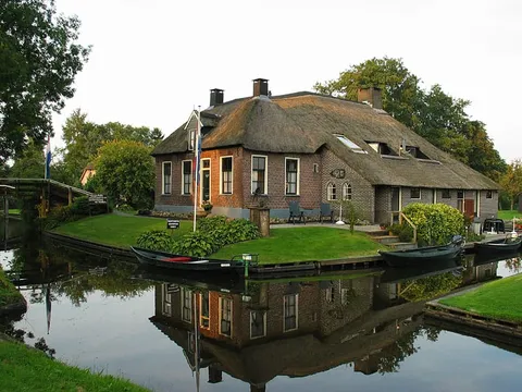 A thatched-roof house reflected in a canal