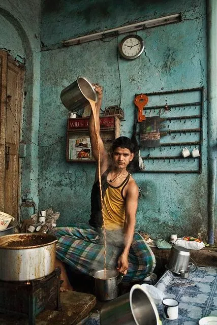 A tea vendor pouring a long stream of tea between metal vessels