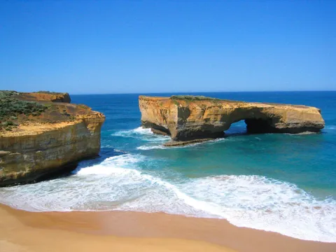 A natural rock arch standing in the sea beside a sandy beach