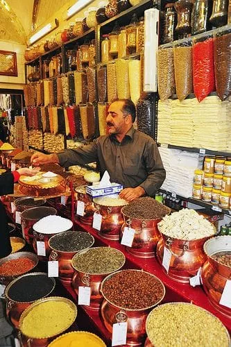A vendor behind bowls of spices in a crowded shop