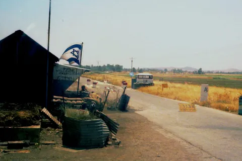 A roadside checkpoint with a barrier, sandbags and an Israeli flag