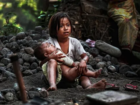 A woman holding a baby beside a pile of stones