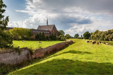 A monastery beyond a brick wall and a wide grassy verge