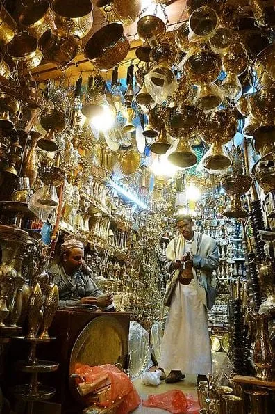 People browsing a shop crowded with hanging metal lamps and vessels
