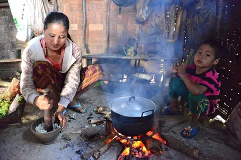 A woman preparing food beside a cooking pot over an open fire