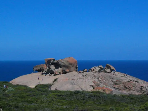 Large weathered boulders on a granite dome by the sea, with visitors