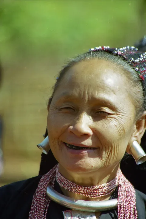A smiling woman wearing large silver earrings, a silver neck ring and beads