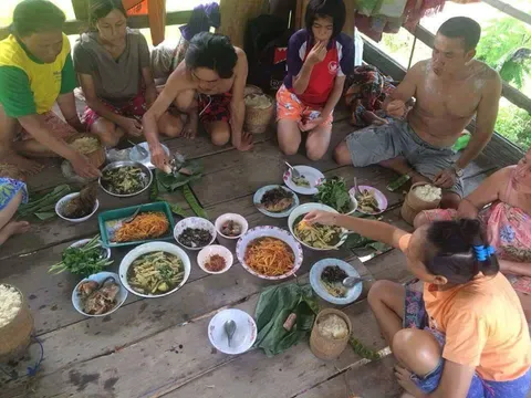 People sitting around many shared dishes on a wooden floor