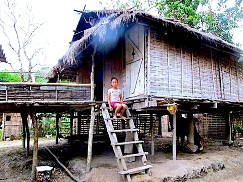 A child sitting on the steps of a raised wooden house
