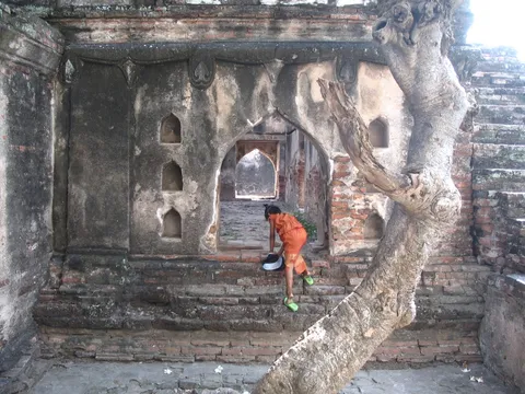A monk in an orange robe climbing steps into a ruined temple doorway