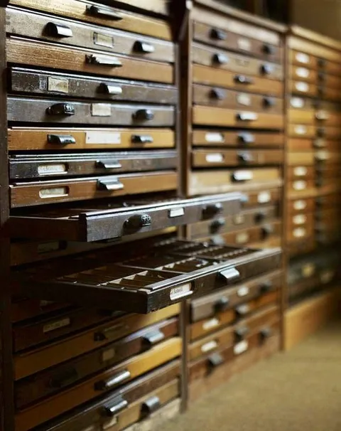Wooden type-case drawers, some pulled open, in a tall storage cabinet