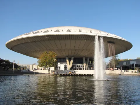 A broad saucer-shaped building supported above a reflecting pool