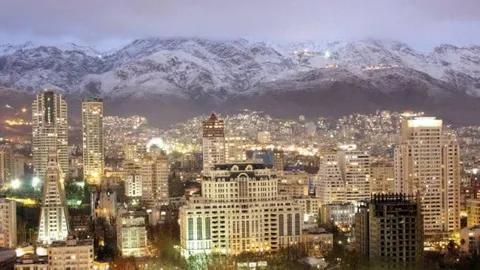 City buildings at dusk below snow-covered mountains