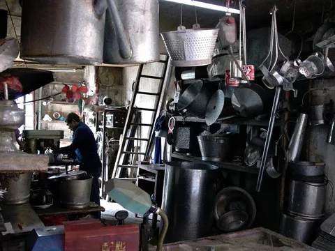 A worker surrounded by large metal pots and vessels in a workshop