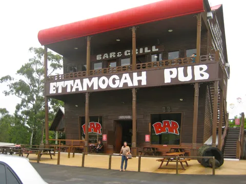 A woman standing outside a two-storey timber pub with a red roof