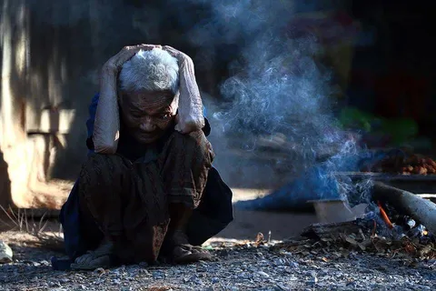 An older person sitting beside a smoky cooking fire