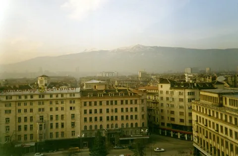 Large city buildings below hazy hills, viewed from an upper window