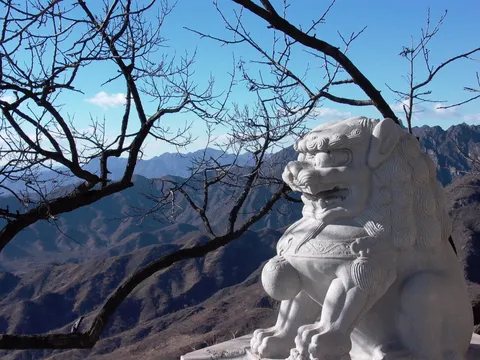 A carved stone lion beside a bare tree overlooking the mountains