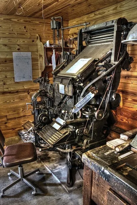 An old metal typesetting machine with a sloping keyboard and exposed mechanisms