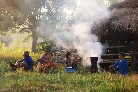 People gathered beside a smoky cooking fire near a rural house
