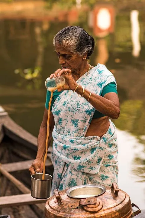A woman pouring tea between small metal vessels at a street stall
