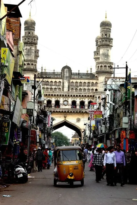 A four-towered monument above a busy street with an auto-rickshaw