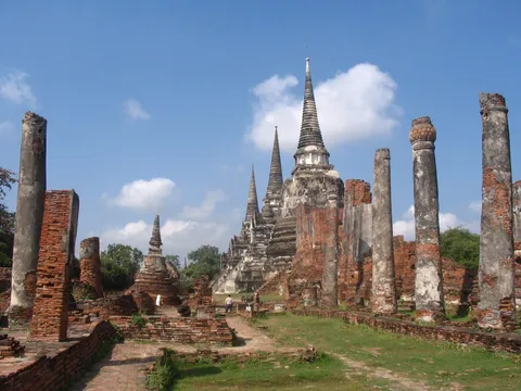 A pointed temple tower and tall stone columns among brick ruins