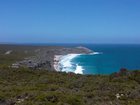 A curved sandy beach below scrubby coastal cliffs and a rocky point