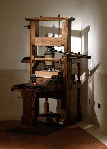 A tall wooden screw printing press displayed against a plain wall