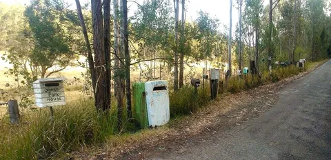 A row of assorted rural letterboxes along a quiet road lined with trees